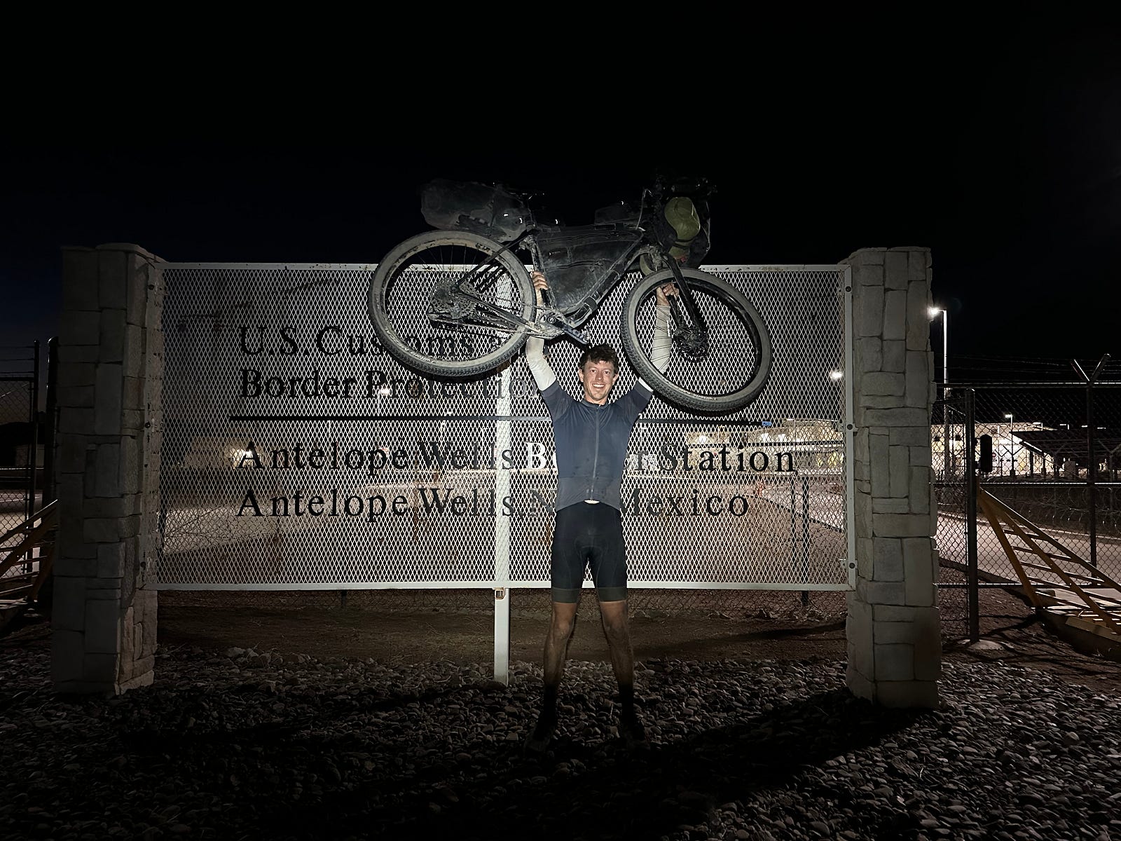 Tim Snyder holding his bike overhead at the Tour Divide finish in Antelope Wells, New Mexico